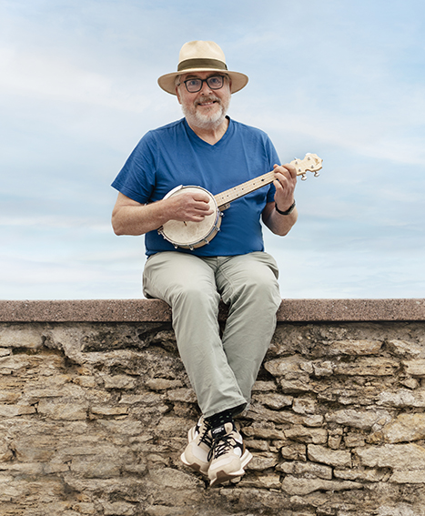 Peter Beckhaus - Experte für handgezeichnete Illustrationen - auf einer Mauer sitzend mit Ukulele in der Hand